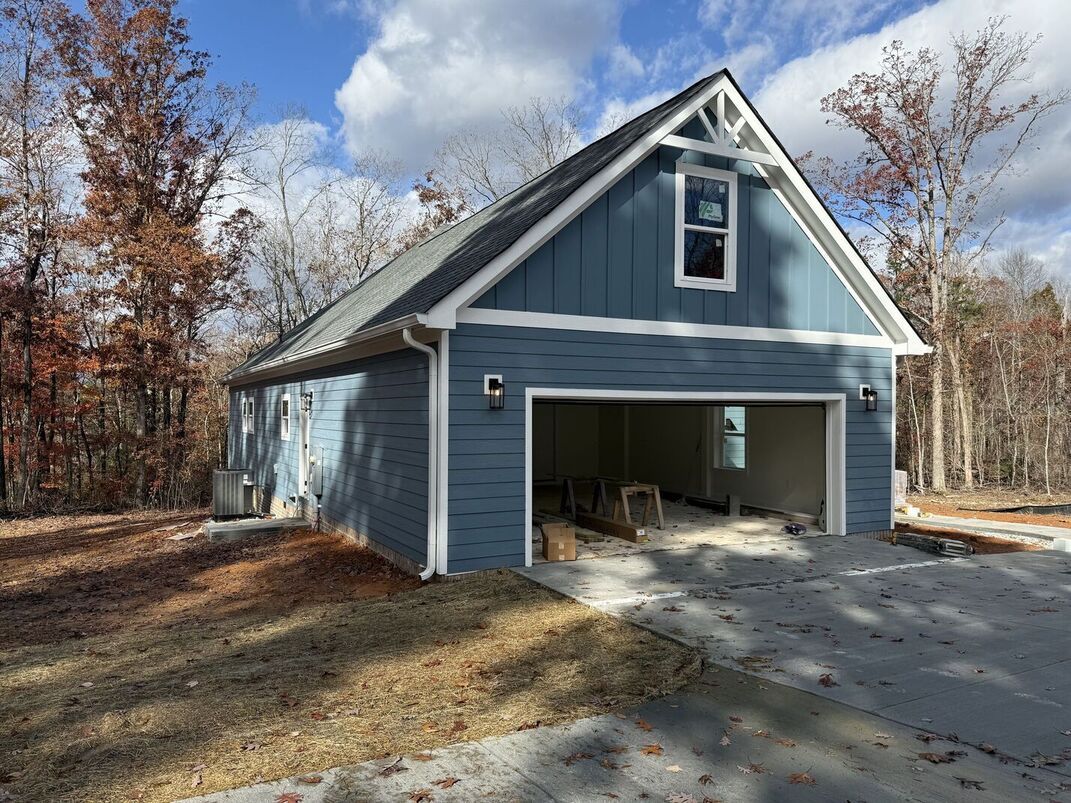 Gray detached garage with open door and driveway in a wooded yard under a blue sky
