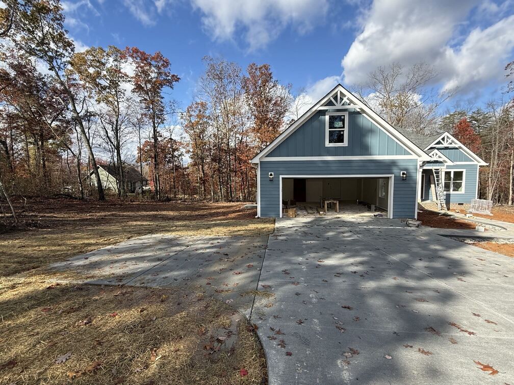 Blue-gray garage with open bay and concrete driveway beside trees under a cloudy sky