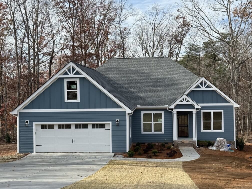Blue suburban house with white trim, two-car garage, and leafless trees in the yard