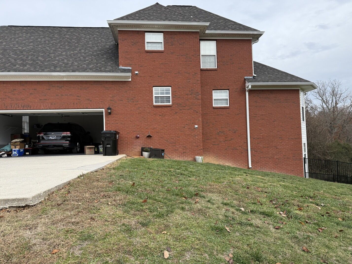 Brick house with open garage, sloped front lawn, and overcast sky