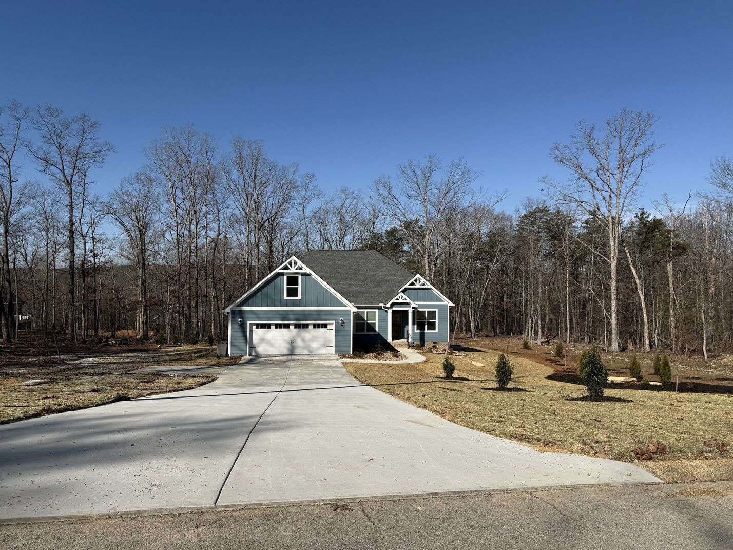 Blue house with white garage and long concrete driveway in a wooded yard