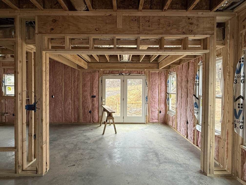Unfinished room under construction with exposed wood framing, concrete floor, and a stool near sliding glass doors