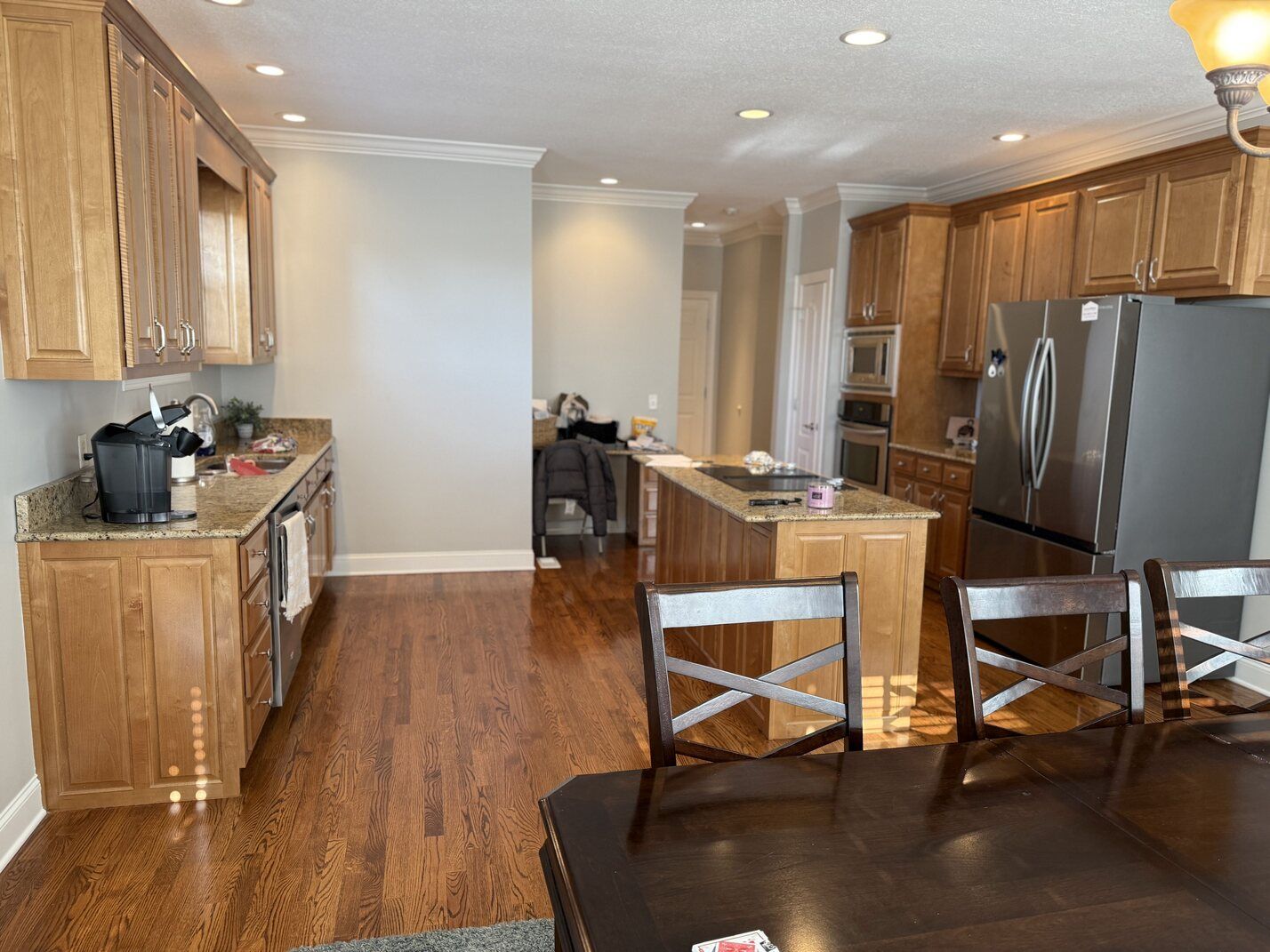 Bright kitchen with wooden cabinets, stainless steel fridge, island, and dark dining table in foreground