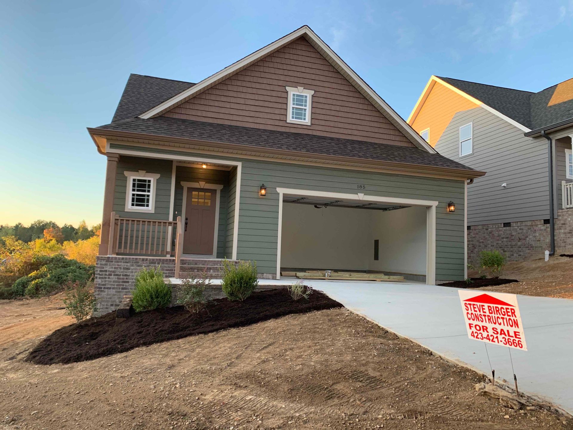 New suburban house with front porch, gray siding, and an open two-car garage at sunset