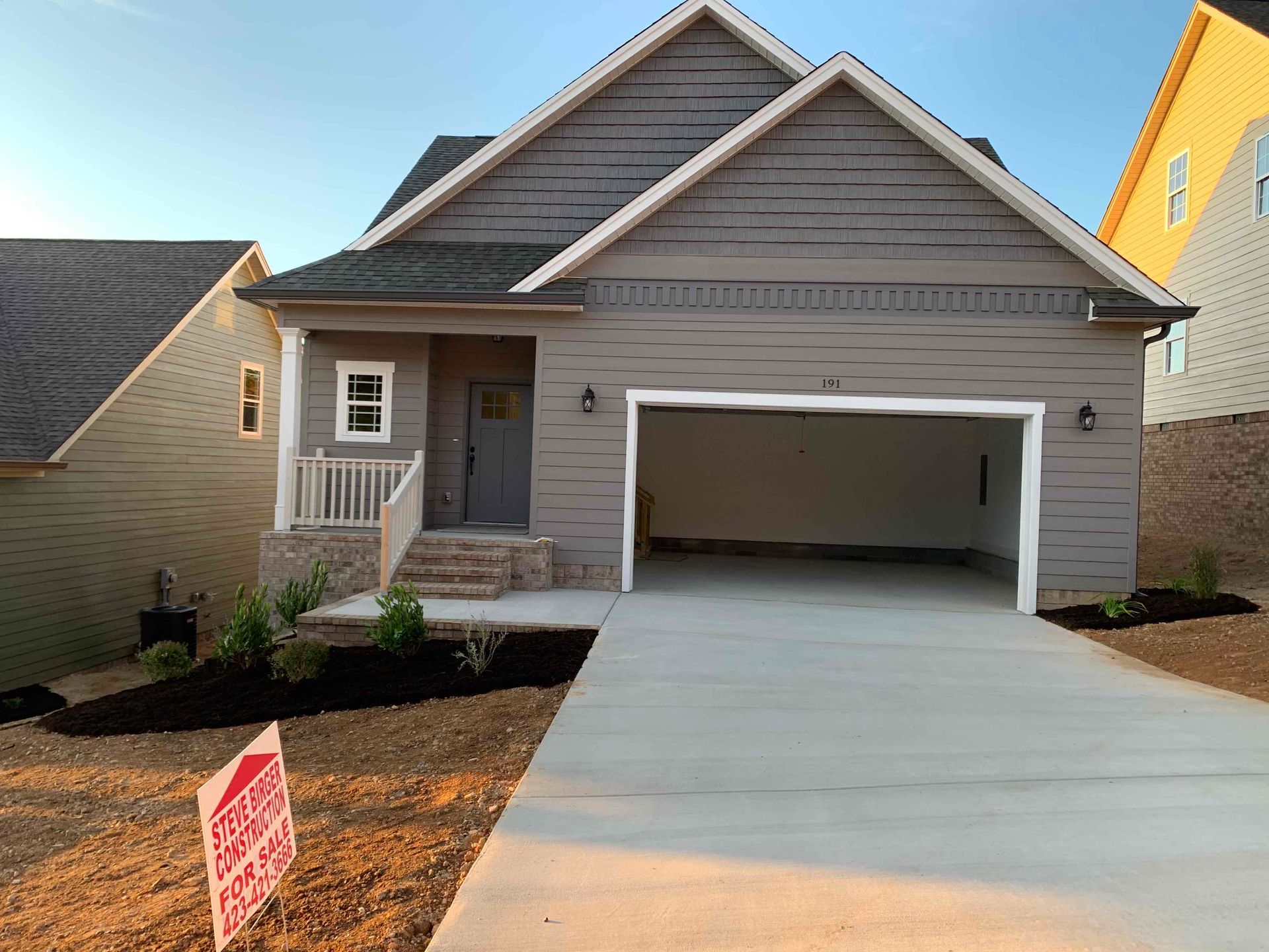 New gray house with front porch and open garage, seen from the driveway