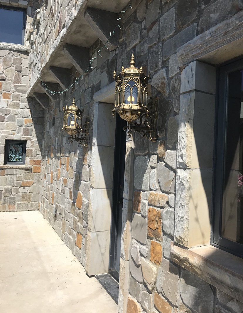 Stone exterior wall with arched bronze gothic lantern sconces and mixed-color masonry around windows and entryway.