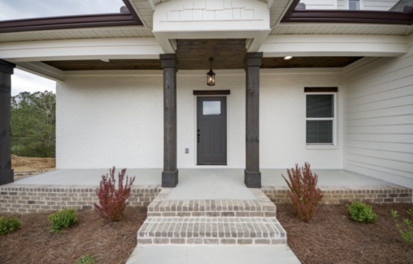 Front entry of a craftsman-style home with white siding, dark wood columns, brick steps, and covered porch with accent lighting.