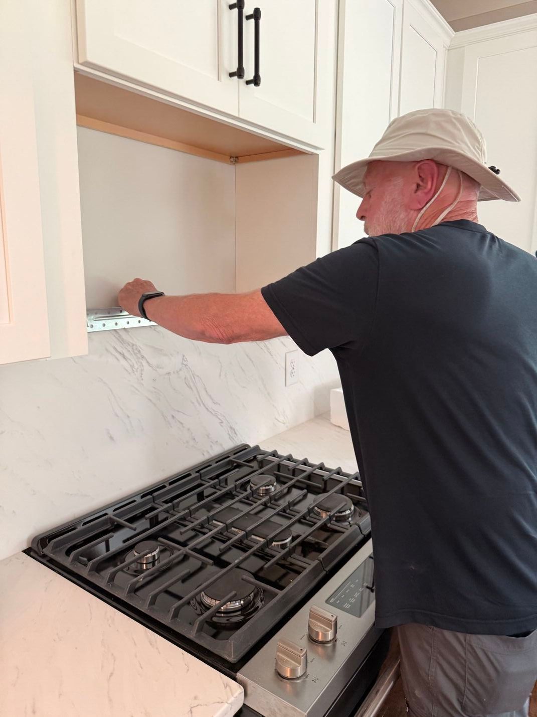 Person installing a backsplash above a gas stove in a white kitchen.