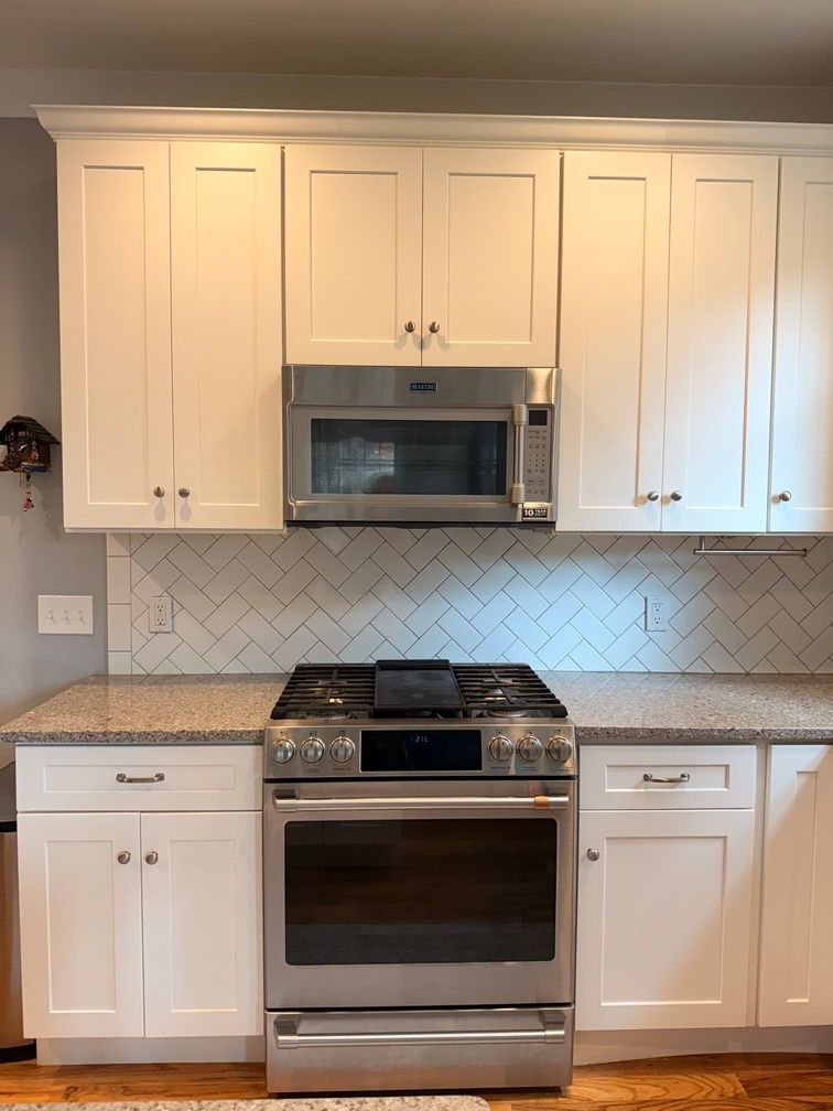 White kitchen with stove, microwave, and cabinets against a light herringbone tile backsplash.