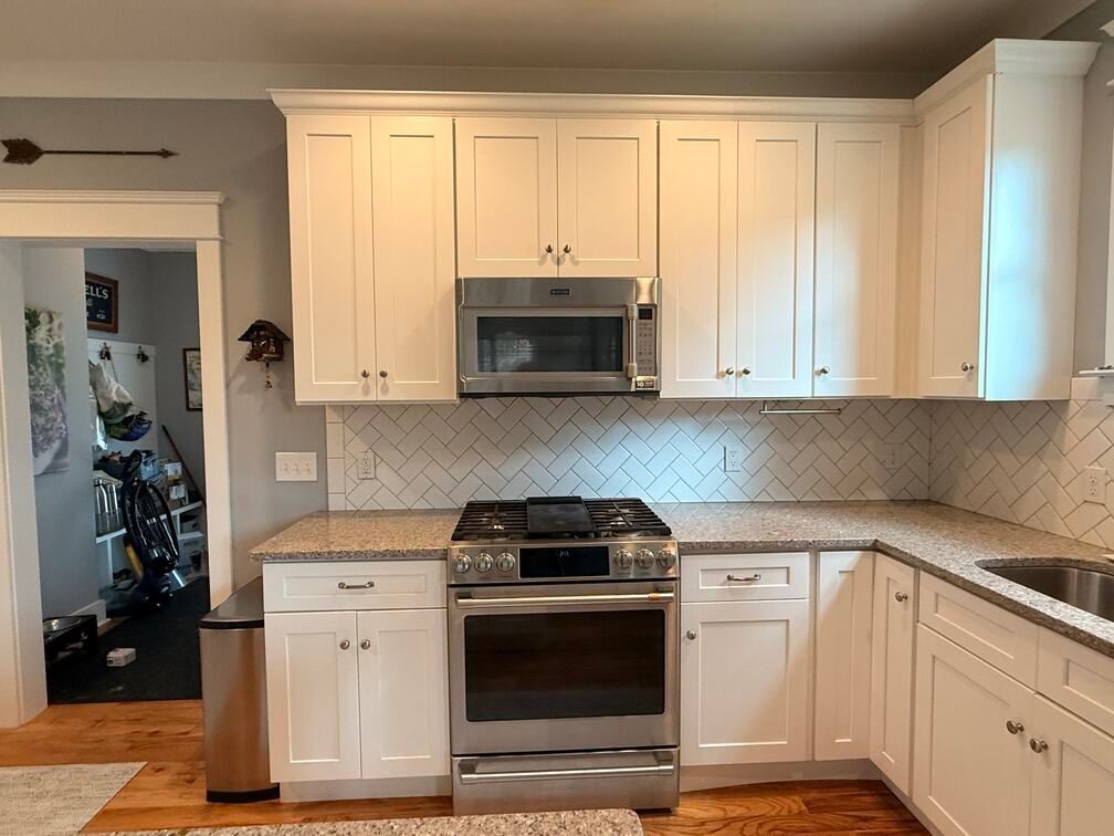 Bright white kitchen with stainless steel stove and microwave, white cabinets, and granite countertops.