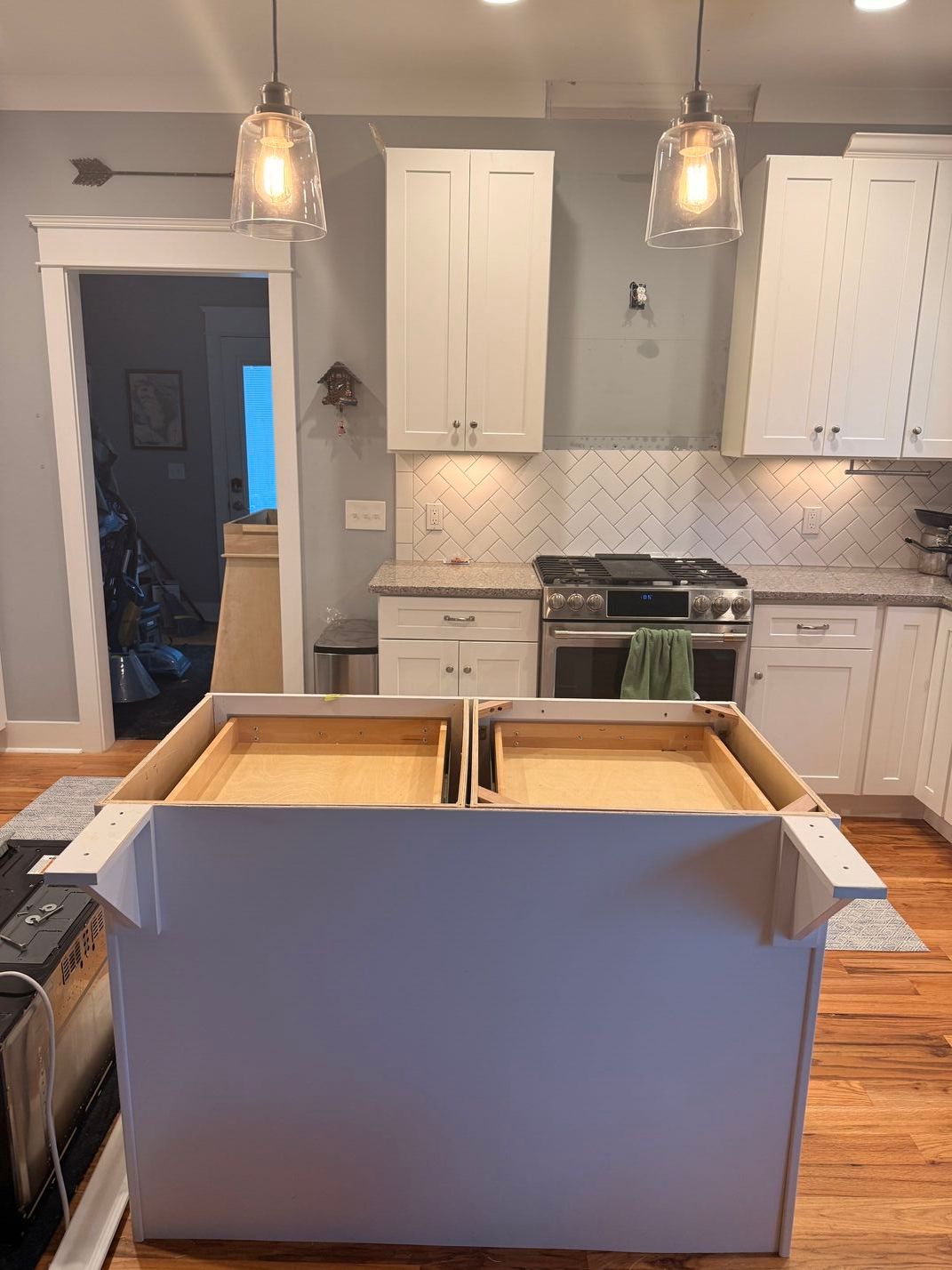 Kitchen with white cabinets and pendant lights, showing an unfinished blue island under construction.