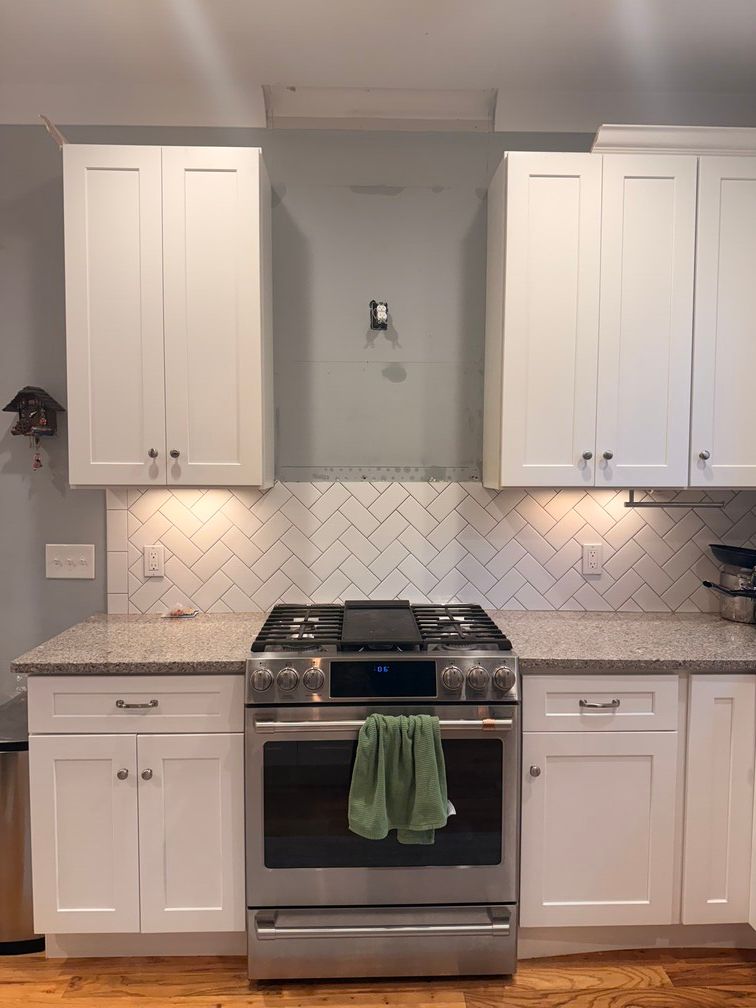 White kitchen with stainless steel range, cabinets, and herringbone tile backsplash