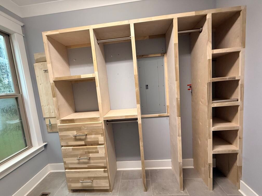 Unfinished wooden closet shelves and drawers installed in a room with a window.