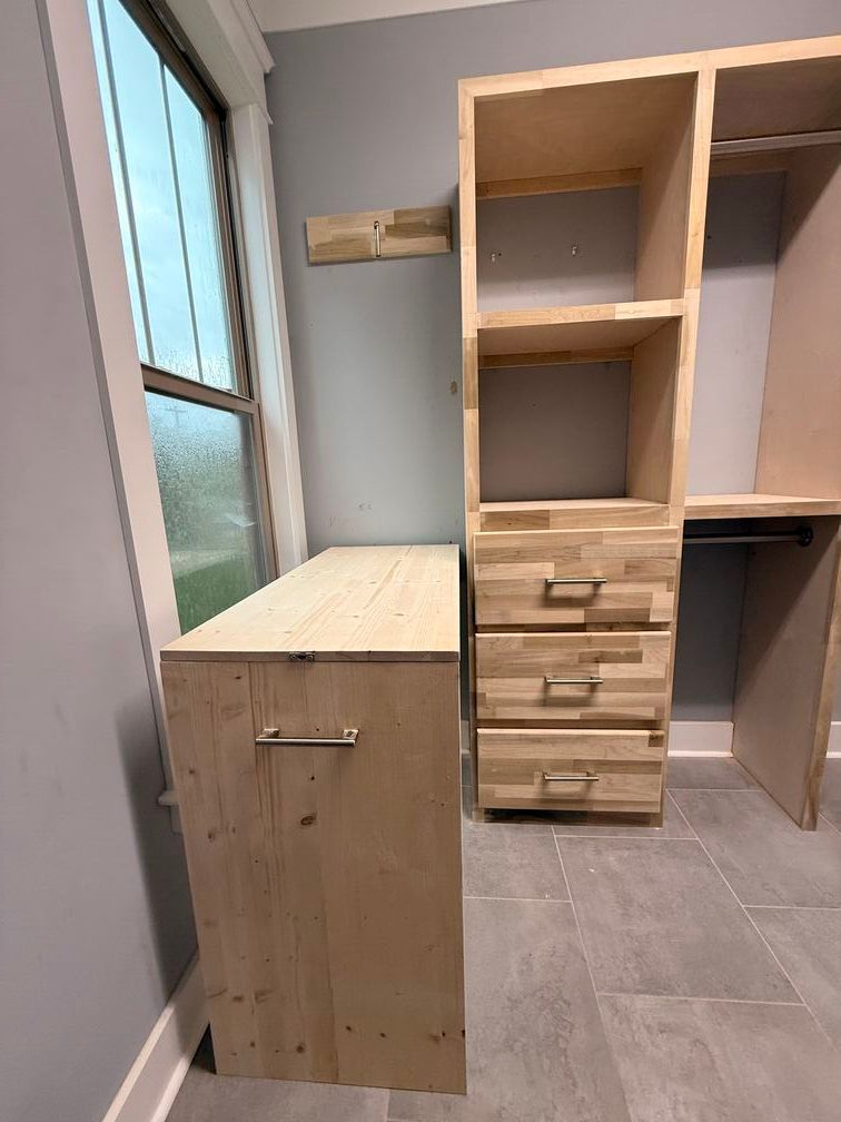Small room with unfinished wooden cabinets and open shelving beside a frosted window.