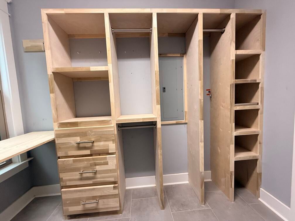 Built-in plywood closet organizer with drawers and shelves in a room, unfinished wood against gray walls