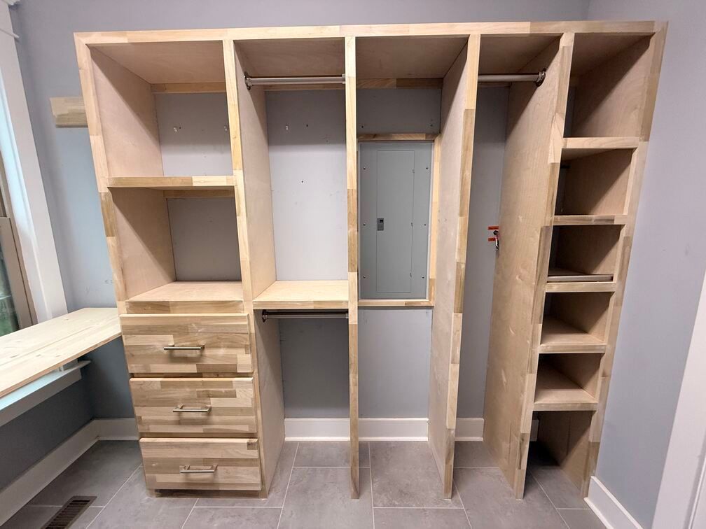 Unfinished wooden closet shelving unit with drawers and open compartments in a room under construction