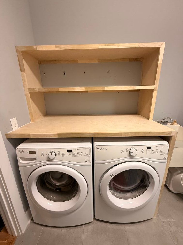 Laundry room with a white washer and dryer beneath unfinished wooden shelves.