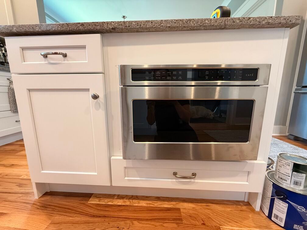 White kitchen cabinet with built-in stainless steel oven and speckled countertop, under counter installation