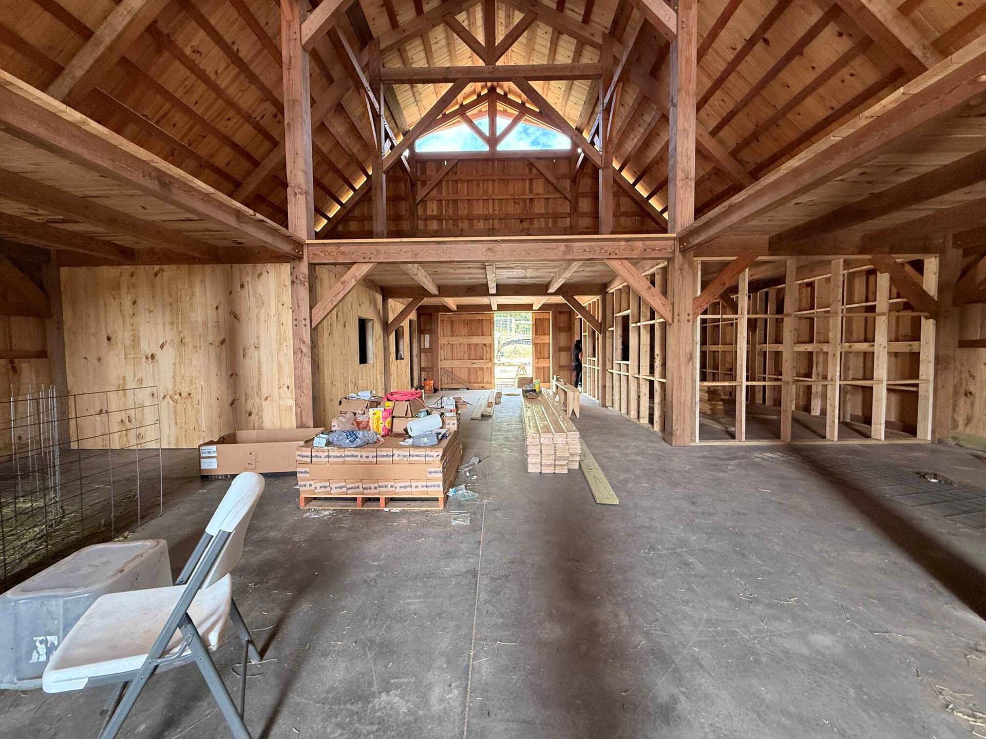 Interior of a wooden barn under construction, with exposed beams, unfinished walls, and building materials stacked inside.