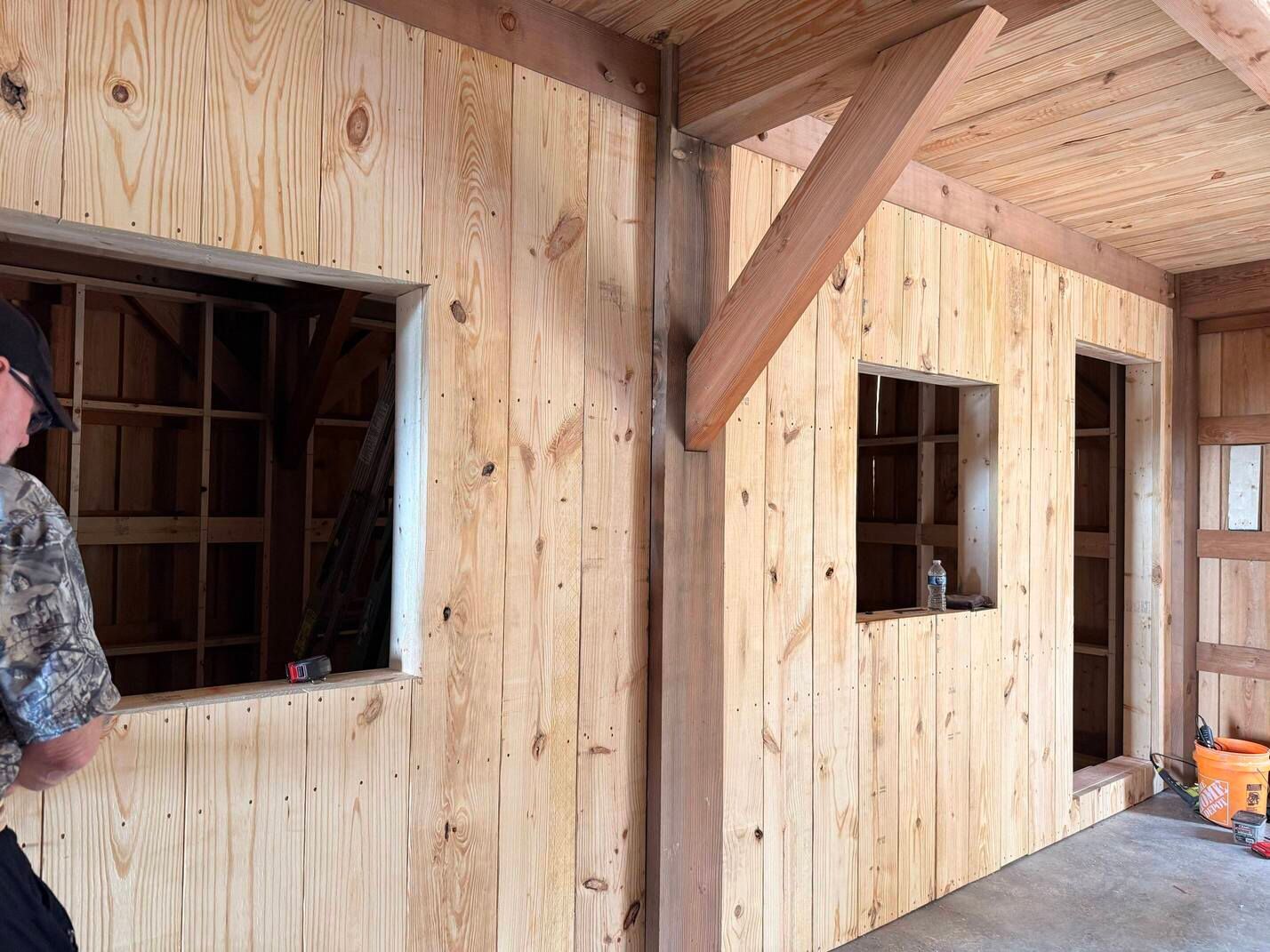 Wood-paneled porch wall with two window openings and a wooden door under construction