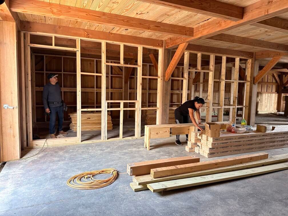 Two workers framing a wooden interior under construction with lumber and tools on the floor