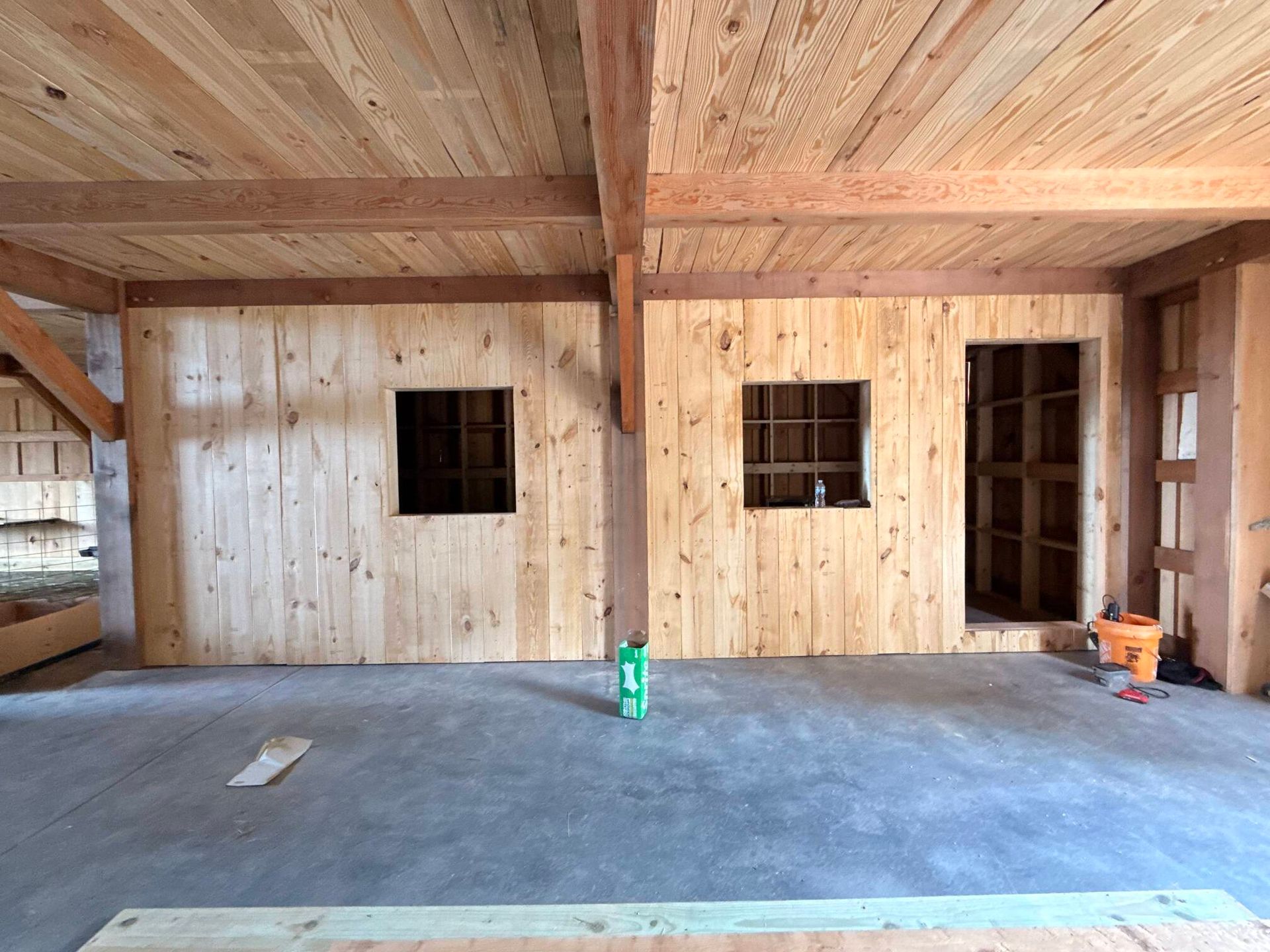 Wood-framed room under construction with plywood walls, concrete floor, and open window and doorway openings.