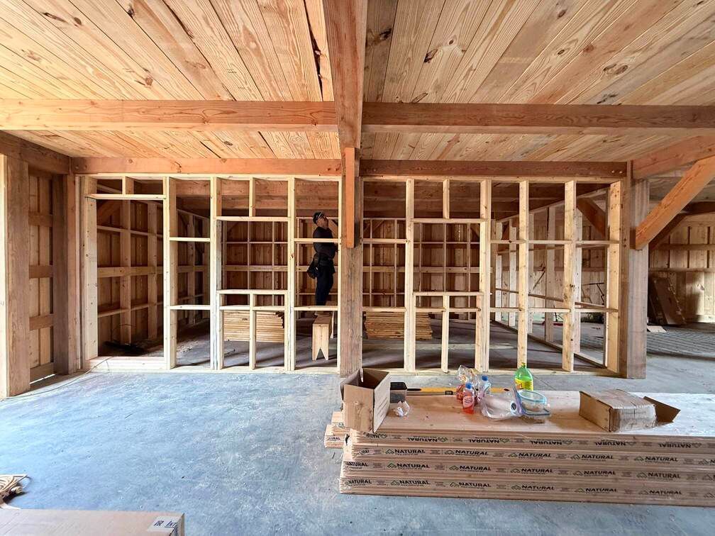 Wood-framed interior under construction with exposed framing, tools, and stacked materials on the floor