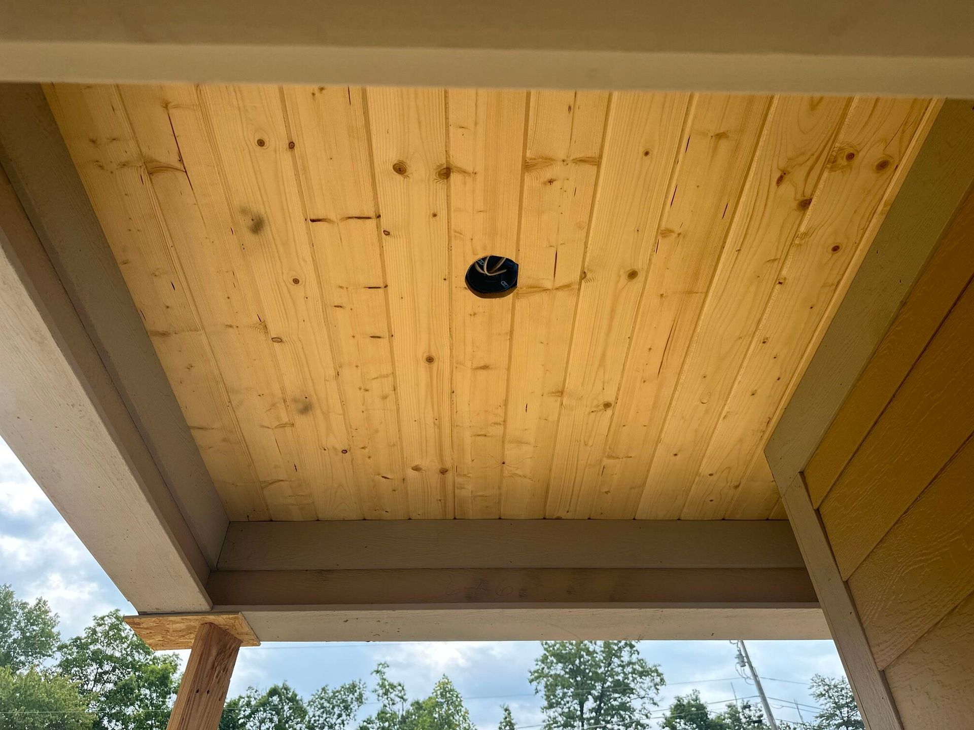 Wood-paneled porch ceiling with a single recessed light opening, viewed from below.