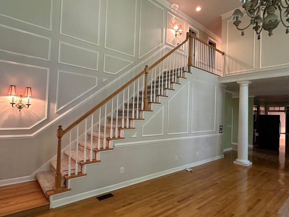 Elegant foyer with a curved staircase, white paneled walls, hardwood floors, and chandelier lighting
