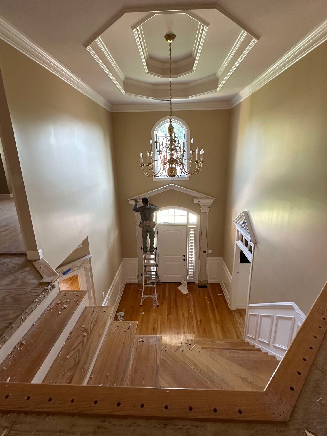 Interior view from an upstairs balcony looking down into a foyer with hardwood floors, beige walls, and chandelier lighting