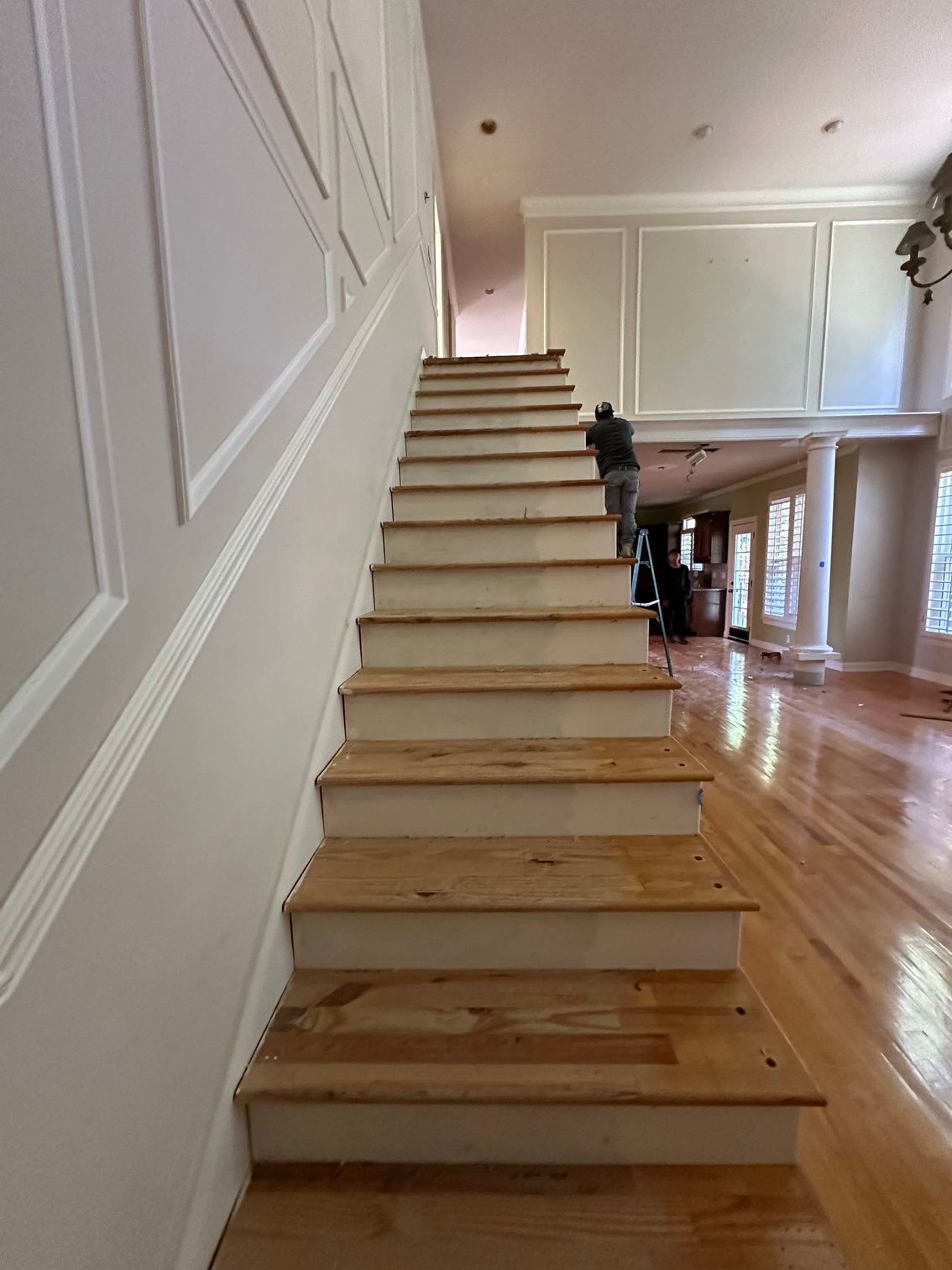 Wooden staircase in a bright home interior with white paneled walls and polished hardwood floors