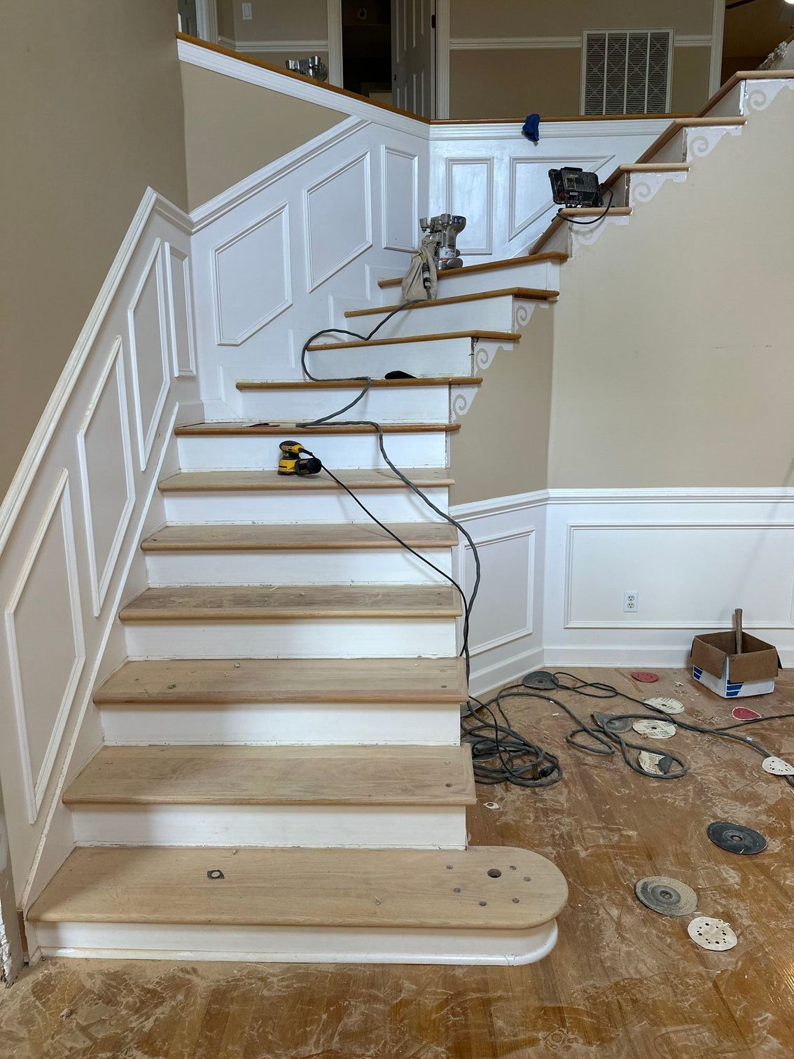 Staircase with white railings and unfinished wooden treads, with tools and construction debris on the floor below