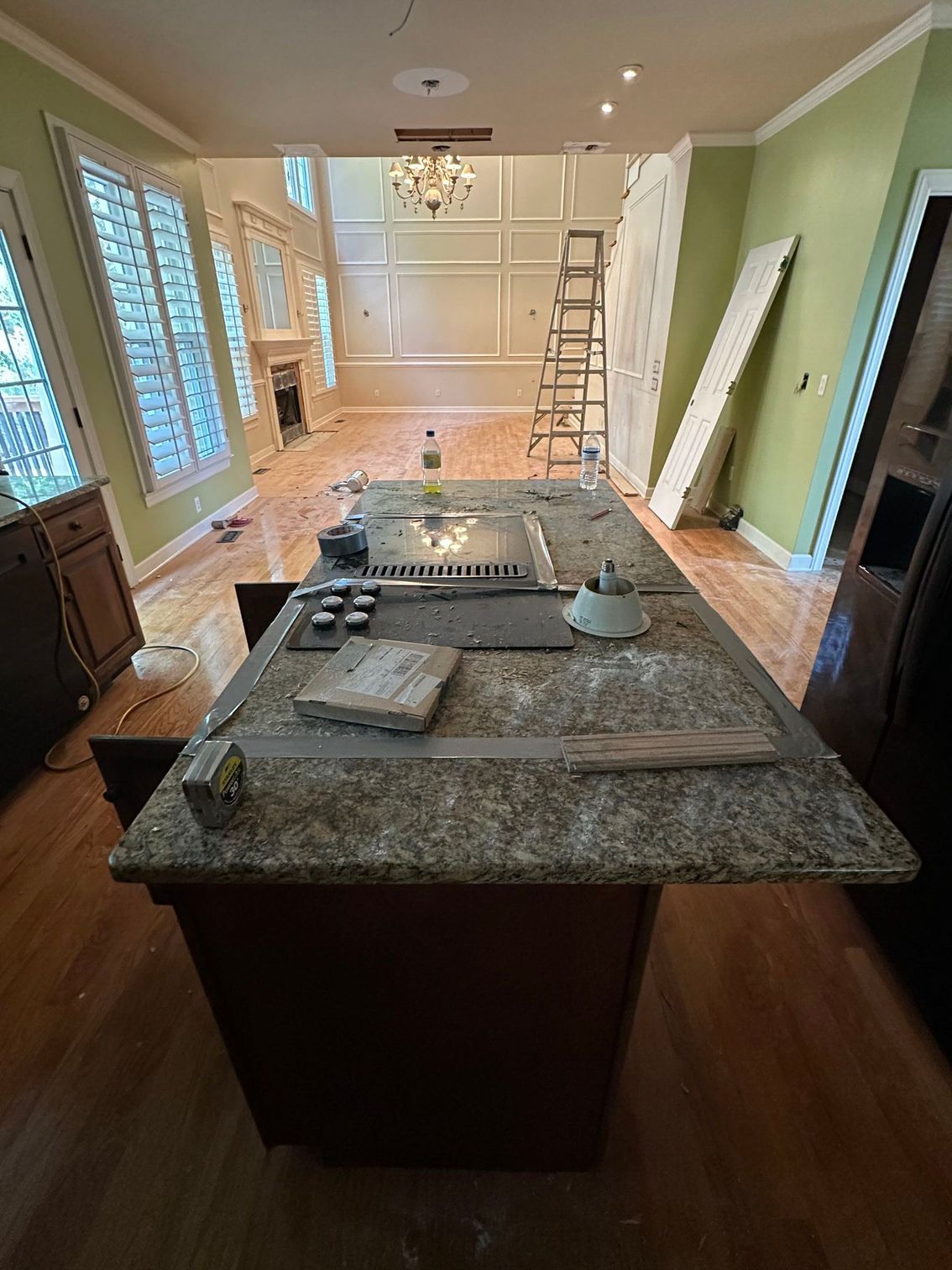 Kitchen under renovation with granite island, open cabinets, ladder, and tools on the floor