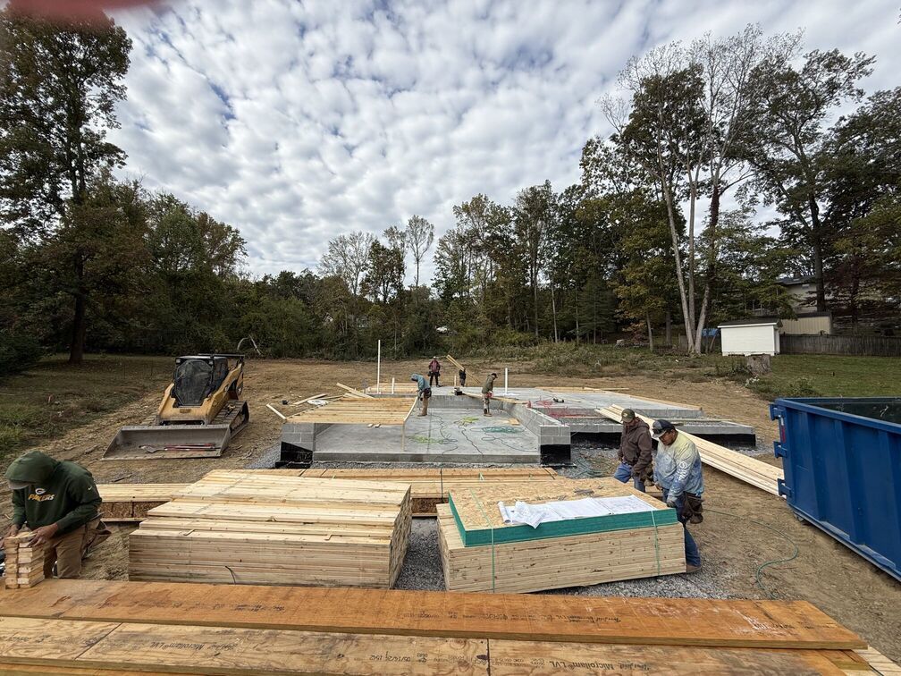Outdoor construction site with wooden forms, workers, and blue barriers under a cloudy sky