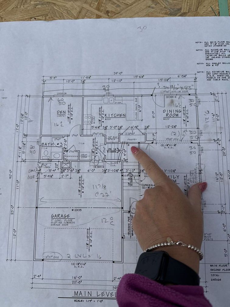 Hand pointing to a printed floor plan with handwritten notes on a white sheet.