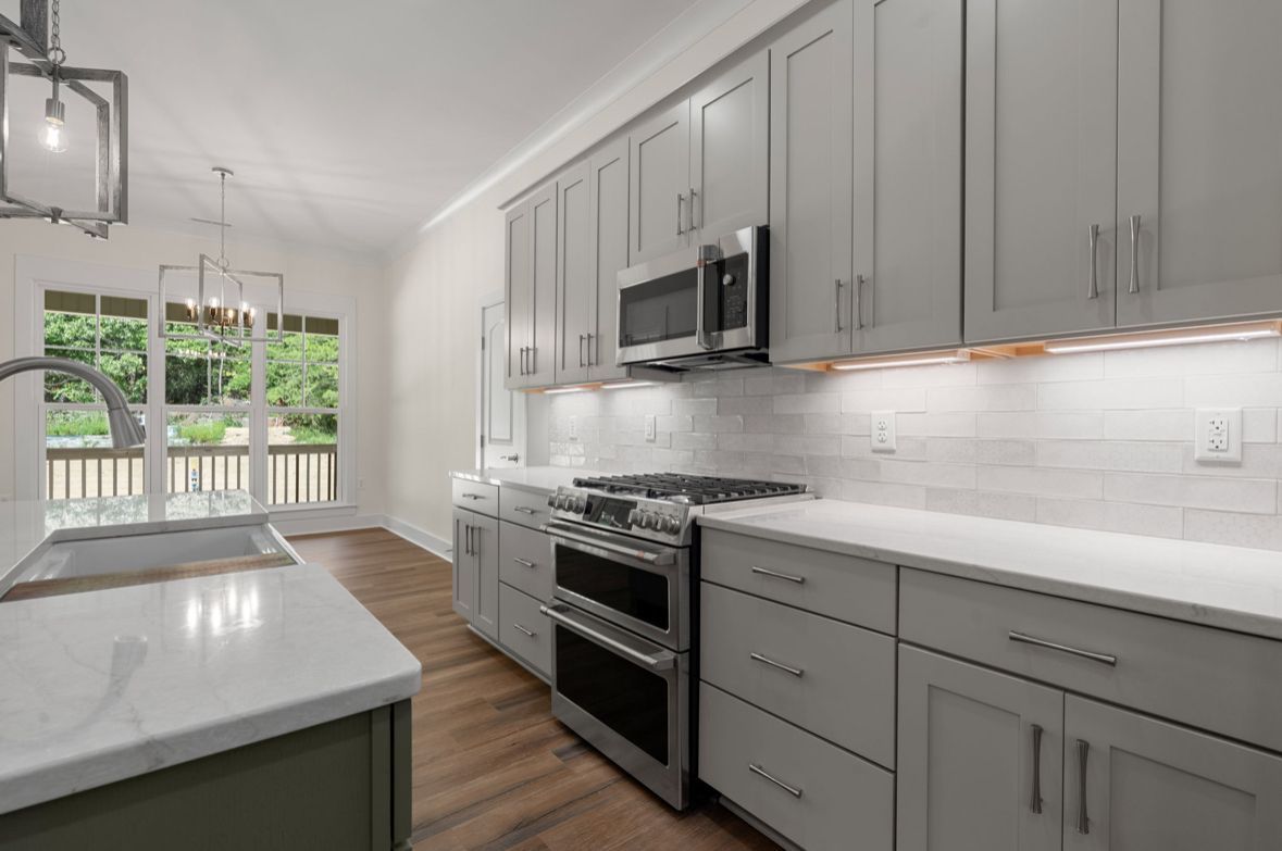 Modern kitchen with gray shaker cabinets, white quartz countertops, and stainless appliances, designed by a custom home builder in Chattanooga.