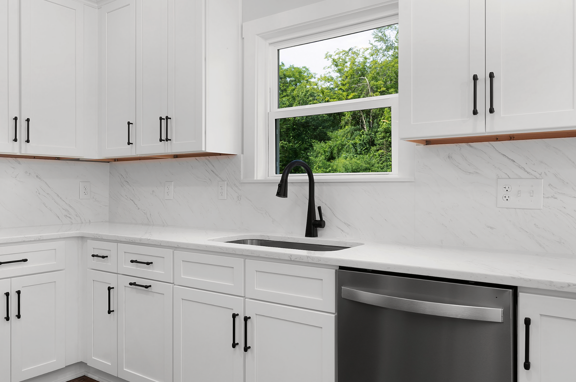 Bright white kitchen with black faucet, marble backsplash, and window above the sink