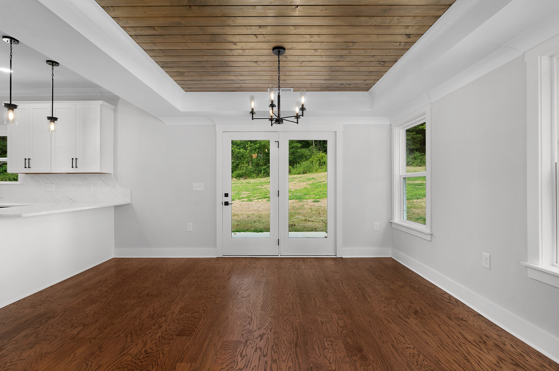 Empty modern living room with wood floor, white walls, wood ceiling, and glass doors to greenery