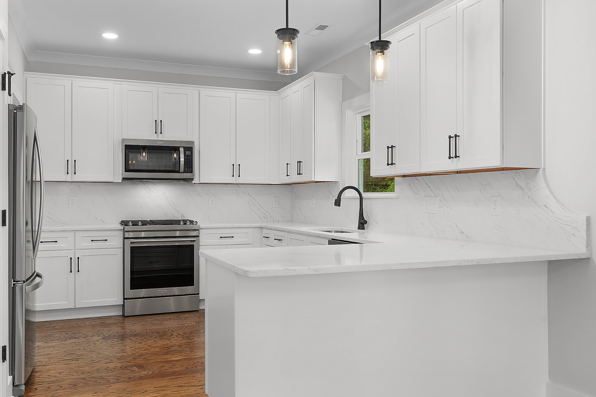 Bright white kitchen with stainless steel appliances, marble counters, island, and pendant lights.