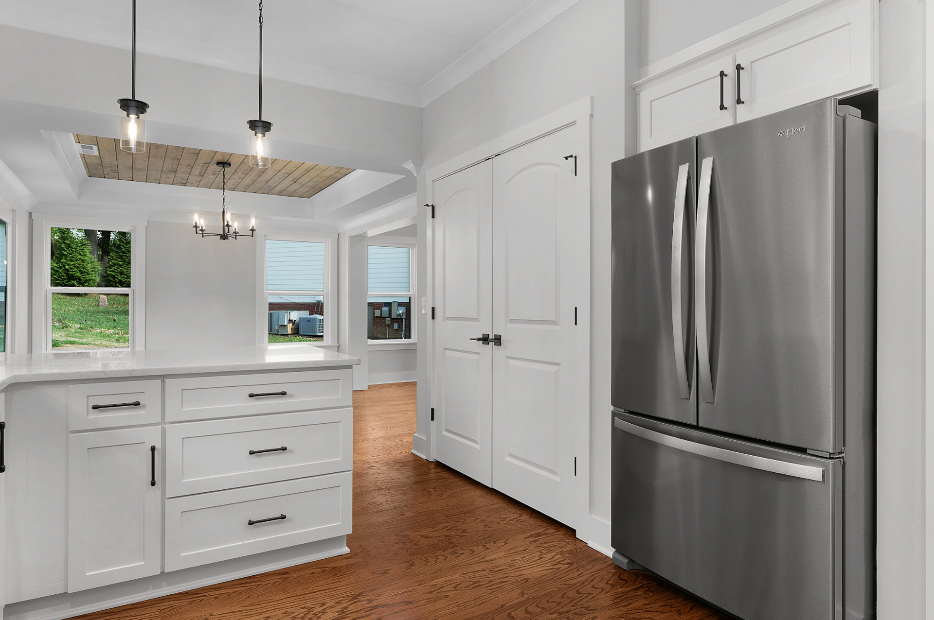 Bright white kitchen with stainless steel fridge, island, and hardwood floors, seen from a doorway.