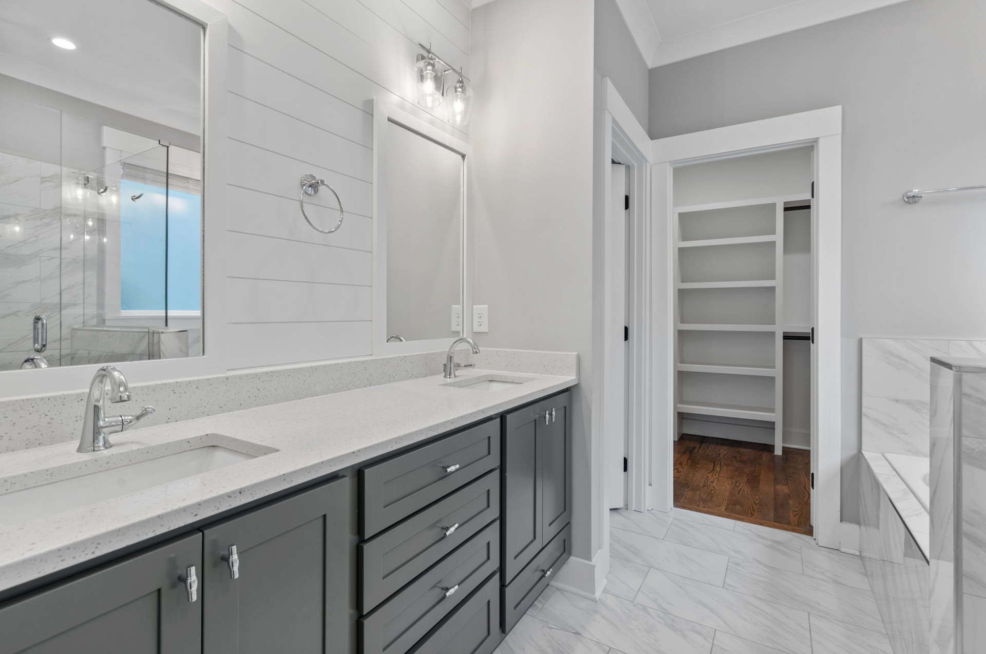 Bright modern bathroom with gray vanity, white marble counters, and open closet doorway.