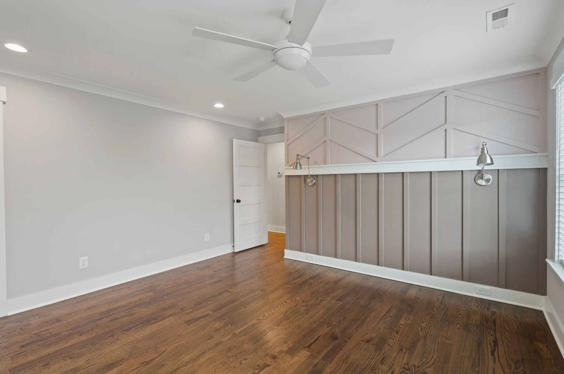 Empty modern living room with wood floors, gray walls, ceiling fan, and decorative paneled accent wall