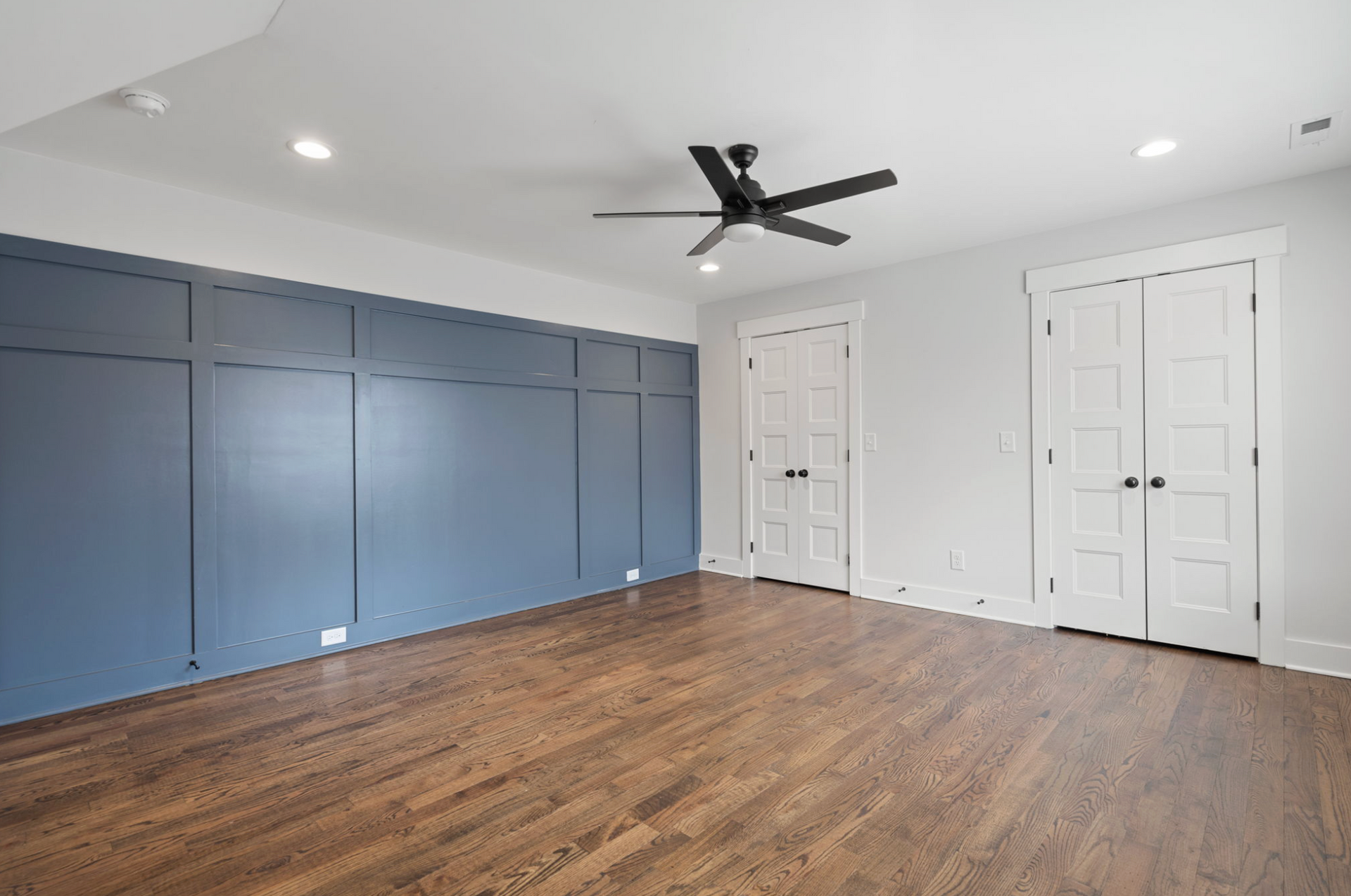Empty bedroom with blue built-in cabinets, white doors, hardwood floors, and a ceiling fan.