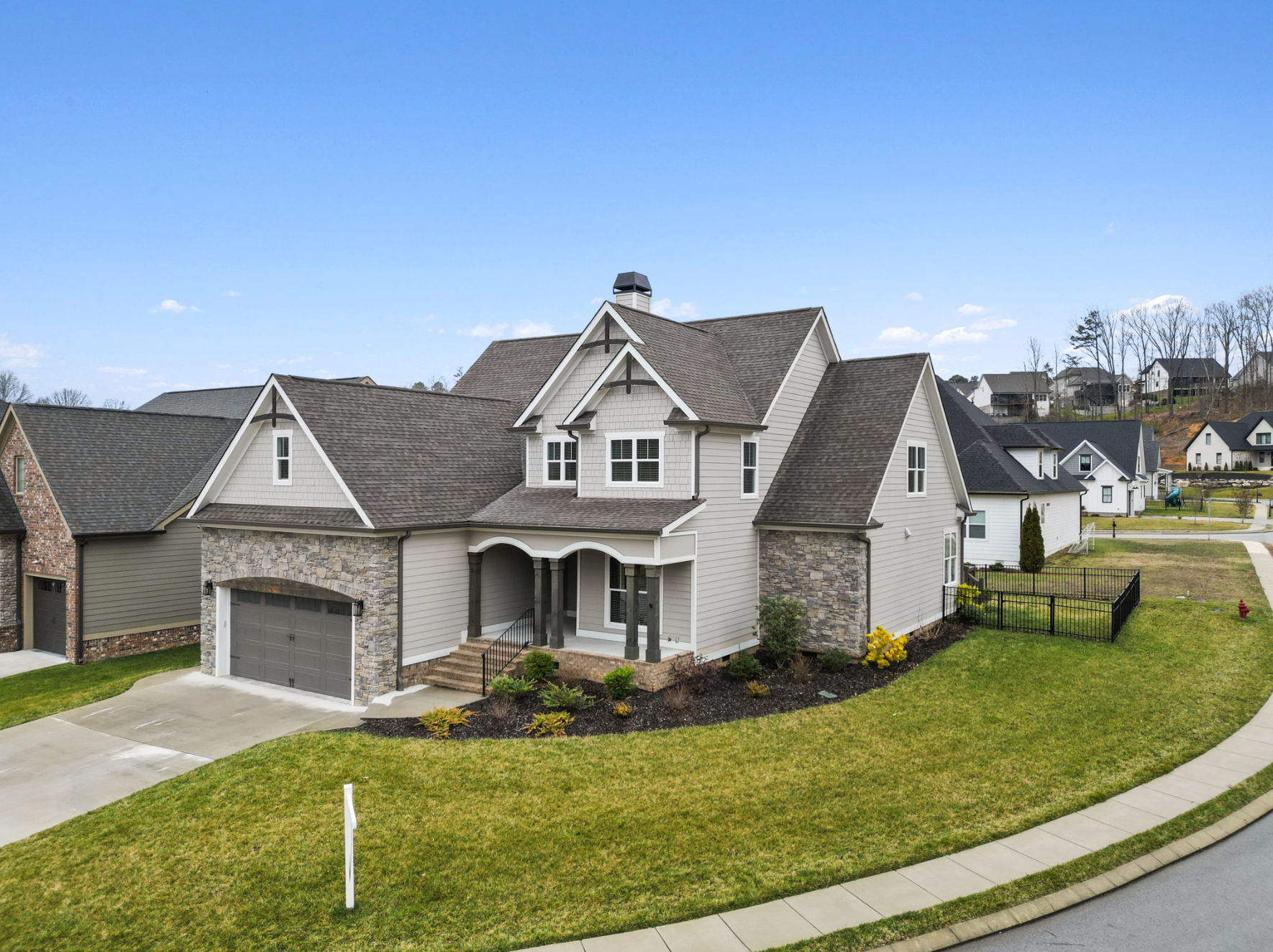 Suburban house with stone facade, attached garage, and manicured lawn on a curved street