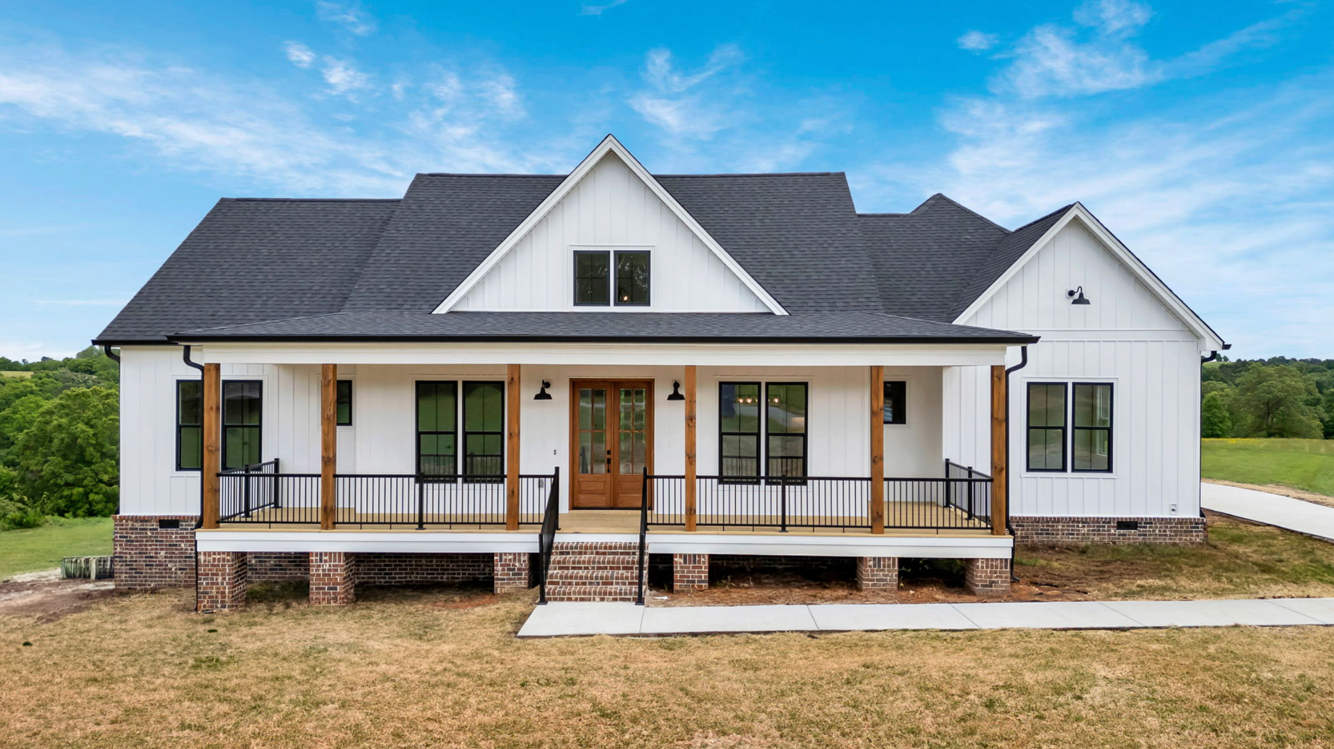White farmhouse with black roof and front porch on a gravel lot under a blue sky