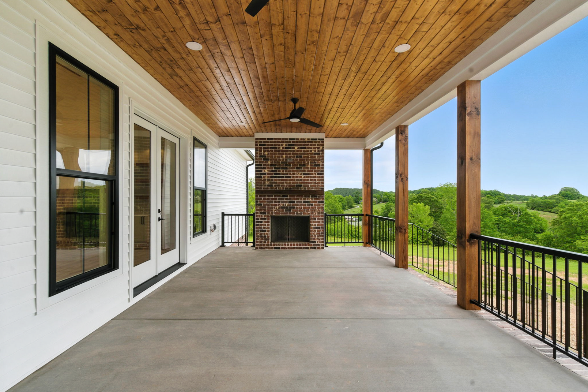 Covered porch with wood ceiling, concrete floor, white walls, black railings, and green landscape view
