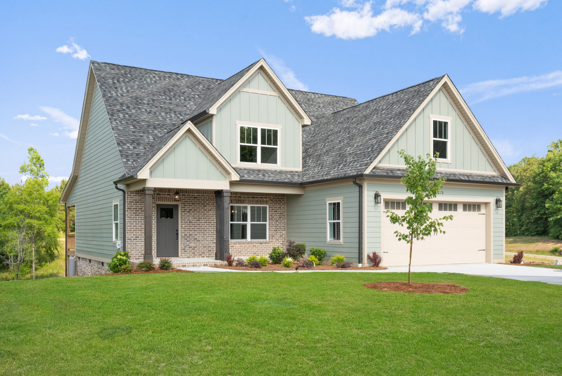Suburban house with gray siding, gabled roof, two-car garage, and a green lawn under a blue sky