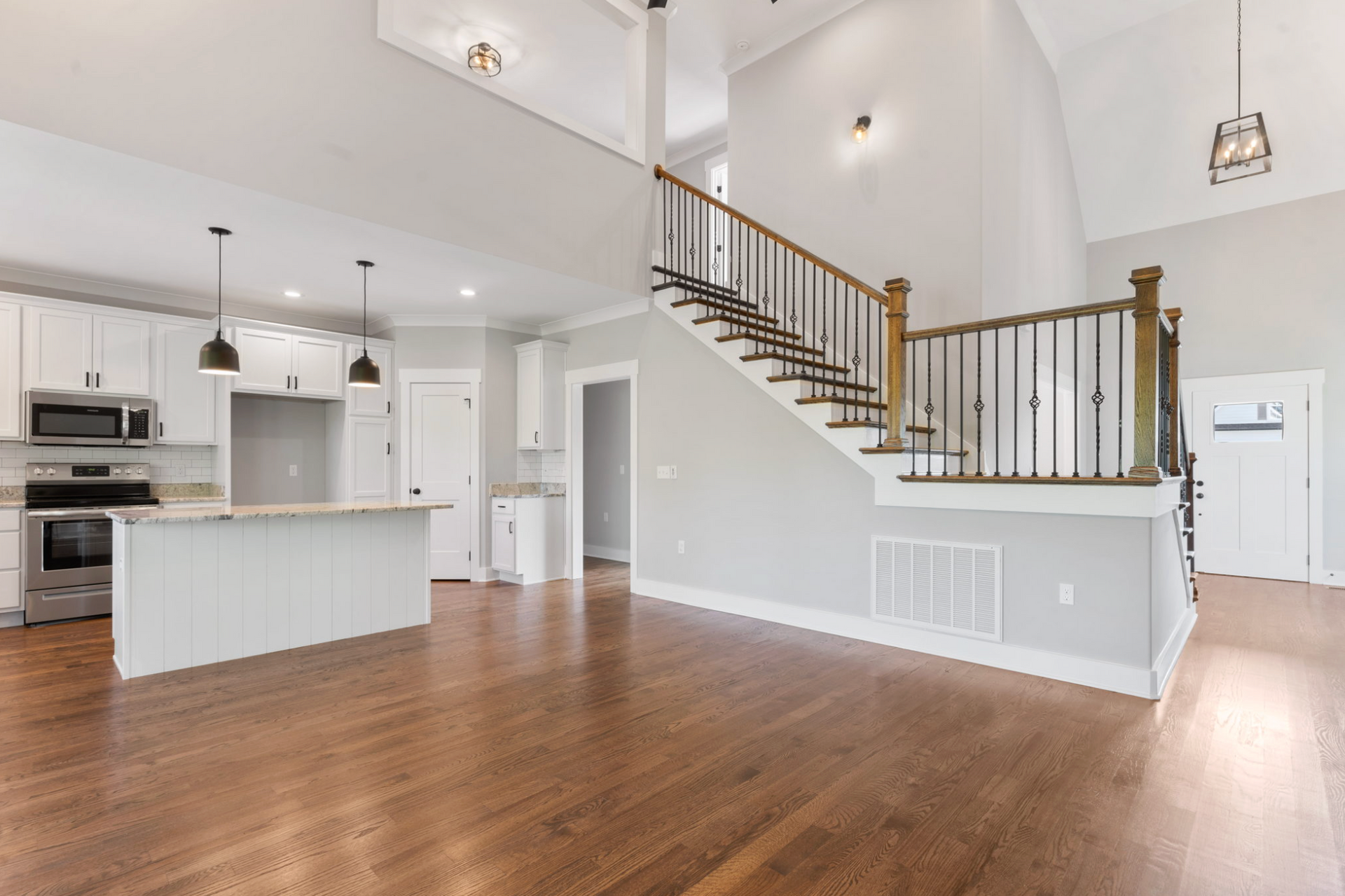 Open-plan living room and kitchen with hardwood floors, white walls, and a staircase with wood railing