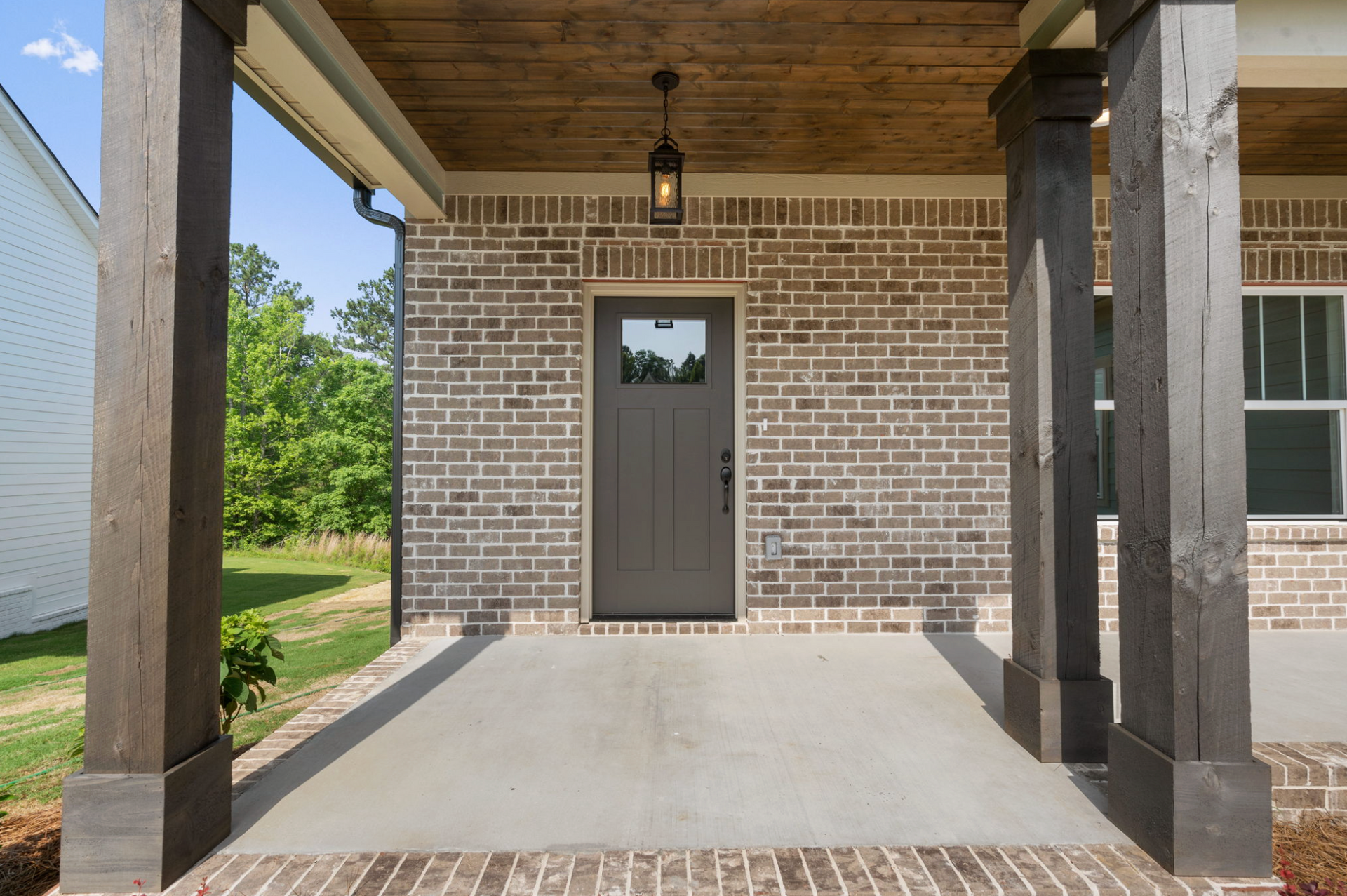 Covered brick front porch with a gray door, wooden posts, and concrete floor