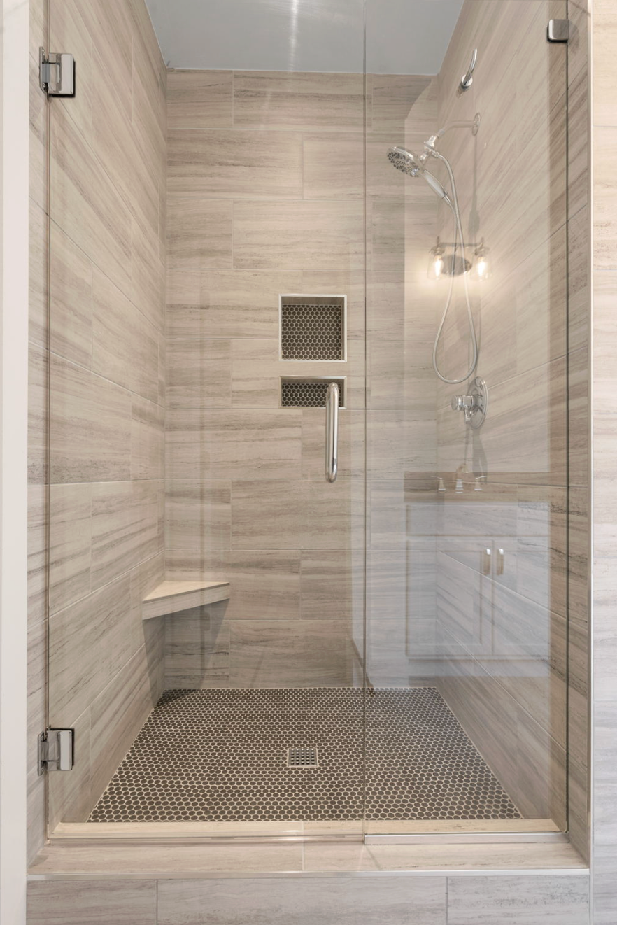 Glass-walled walk-in shower with beige tile, built-in bench, and rain showerhead.